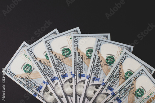 One hundred dollar bills laid out in a semicircle, on a black background.