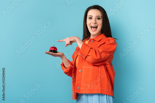 shocked woman pointing with finger at service bell on blue background