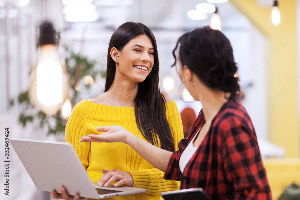 Beautiful girl with long dark hair working on laptop and discussing with her female colleague in a modern business office. Beautiful girl with long dark hair working on laptop and discussing with her female colleague in a modern business office.