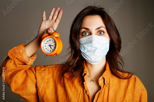 Young woman wearing protecion mask and holding clock in hand photo