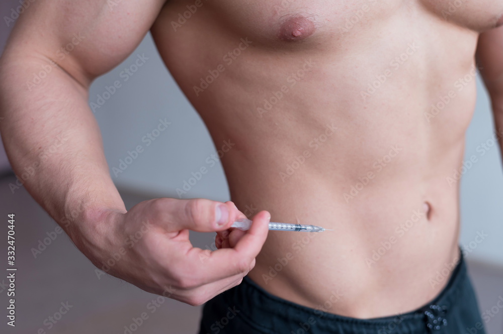 Obraz premium Close-up of a male torso. A shirtless bodybuilder puts a dope shot in his stomach. Faceless athlete puts an injection with illegal drugs.