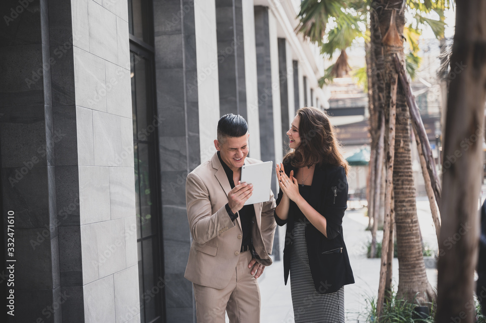 Happy businessman showing content on tablet to female colleague. Business man and woman walking outside Happy businessman showing content on tablet to female colleague. Business man and woman walking outside