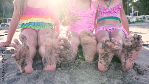 Close up of the feet of three girls sitting on the sand on the beach on a sunny day
