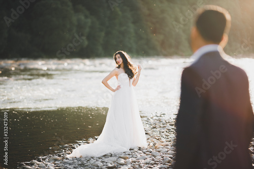 Elegant stylish happy blonde bride and gorgeous groom on the background of a beautiful river in the mountains © olegparylyak