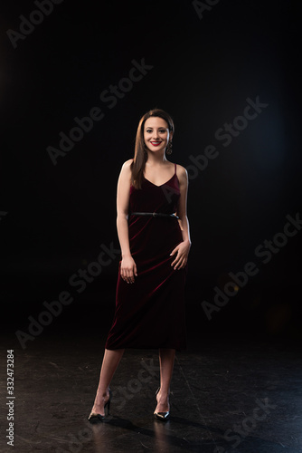 smiling woman in dress looking at camera on black background