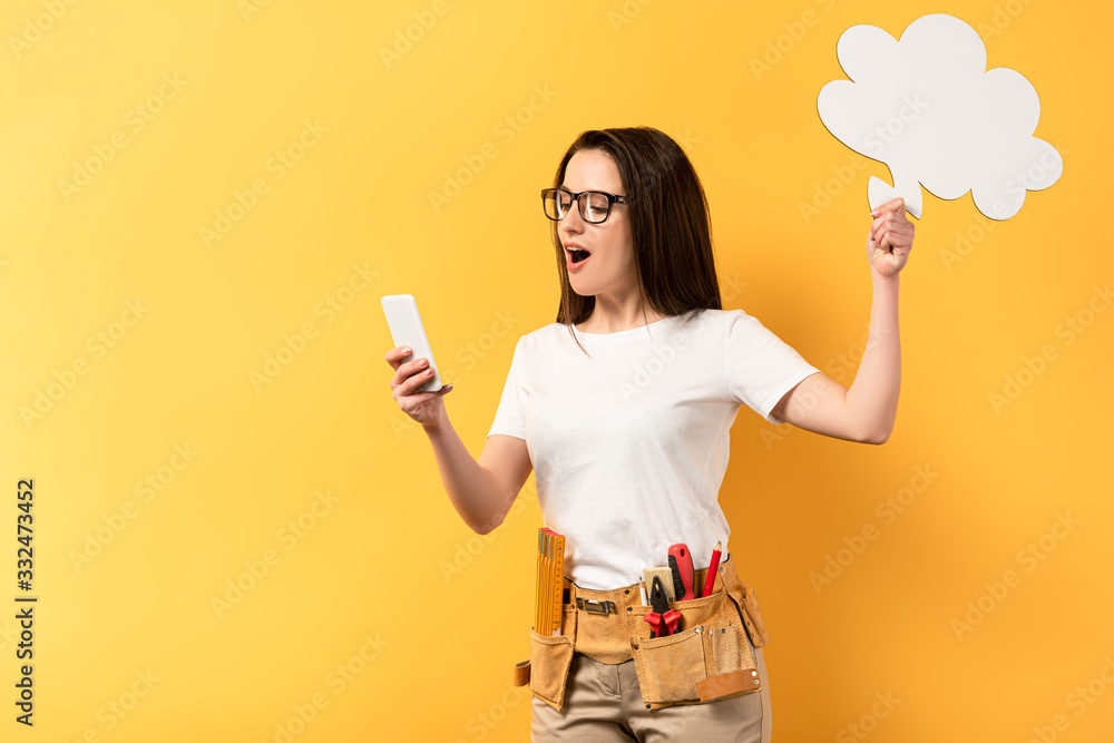 shocked repairwoman holding thought bubble and using smartphone on yellow background shocked repairwoman holding thought bubble and using smartphone on yellow background