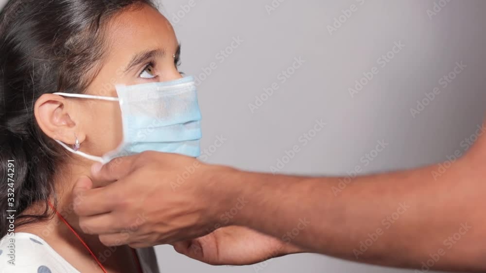 Prevention of spreading the coronavirus or COVID-19 outbreak by wearing mask - Father wearing a disposable hygienic face mask to his young girl daughter to protect spread of disease. Prevention of spreading the coronavirus or COVID-19 outbreak by wearing mask - Father wearing a disposable hygienic face mask to his young girl daughter to protect spread of disease.