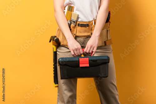 cropped view of handywoman holding toolbox on yellow background photo