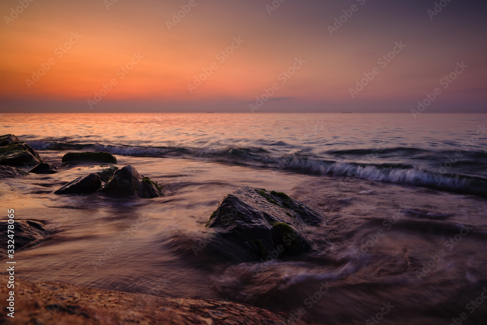 Sunrise at sea. Stones, waves and the sun. Seascape.