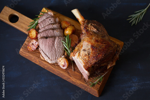 Fotografia, Obraz Roast leg of lamb with potatoes and rosemary on dark background