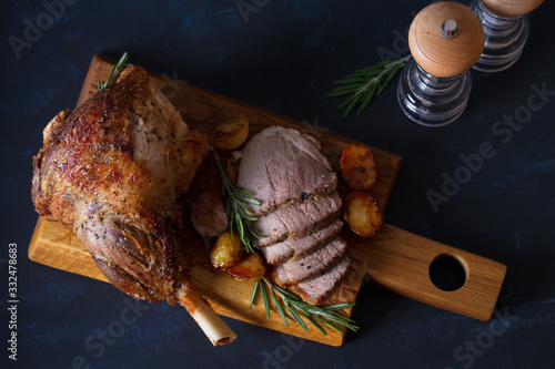 Roast leg of lamb with potatoes and rosemary on dark background. Overhead, flat lay, horizontal image