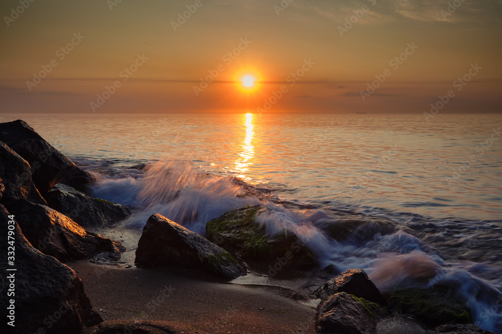 Sunrise at sea. Stones, waves and the sun. Seascape.