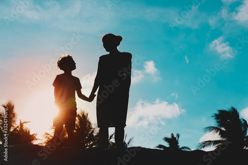 silhouettes of mother and son holding hands at sunset