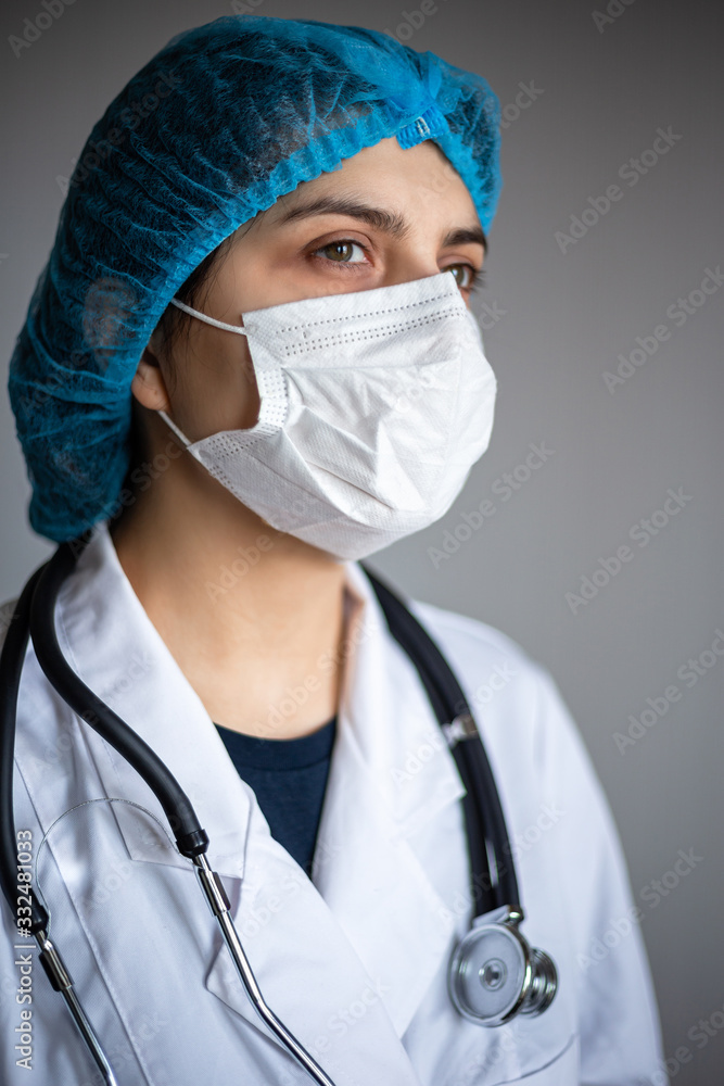 Angle portrait of a young female doctor wearing medical mask, gown and stethoscope. Nurse waiting for the next patient at a hospital for usual check. Coronavirus prevention and doctor visit concept. Angle portrait of a young female doctor wearing medical mask, gown and stethoscope. Nurse waiting for the next patient at a hospital for usual check. Coronavirus prevention and doctor visit concept.