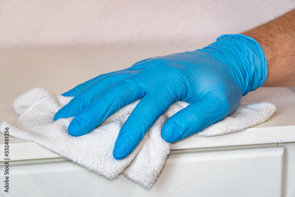 A man in protective blue gloves washes the furniture on the nightstand with a rag. Prevent the spread of coronavirus and infection COVID-19