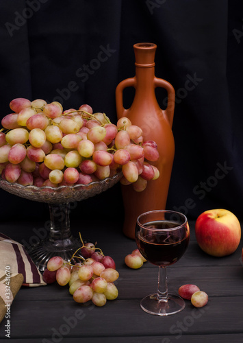Red wine in a glass with grapes in a vase on a wooden table on a black cloth background with an old bottle. For wine advertising