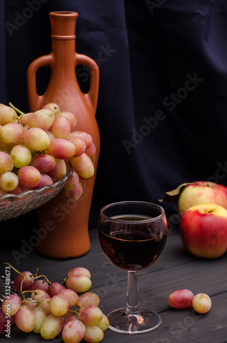 Red wine in a glass with grapes in a vase on a wooden table on a black cloth background with an old bottle. For wine advertising