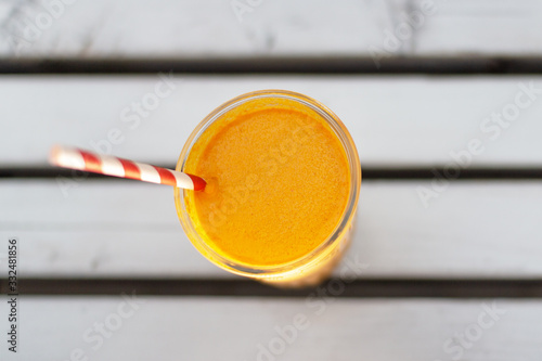 Appetizing thick orange color smoothie close-up with a red and white eco straw on a white wooden table.