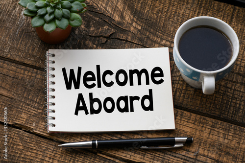 Fotografi WELCOME ABOARD text inscribed in the notebook on a wooden table.