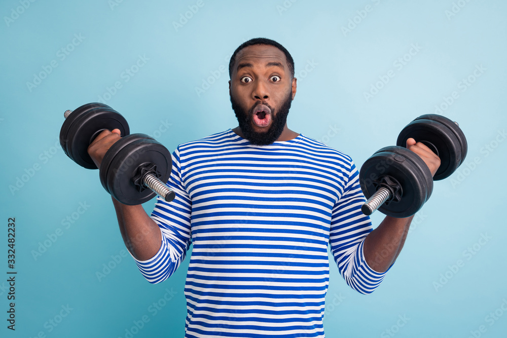 Photo of handsome dark skin guy open mouth lifting two heavy dumbbells weight practicing hard gym strong arms wear striped sailor shirt isolated blue color background