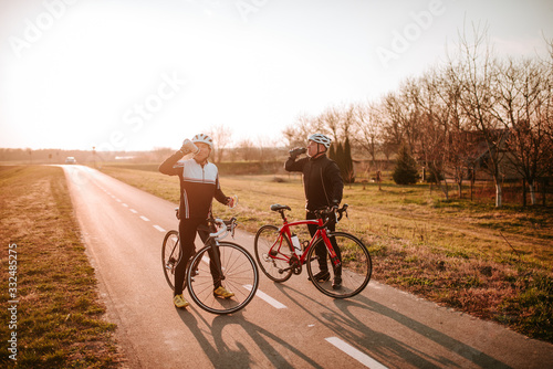  Two middle-aged cyclists drink water on the road. Resting