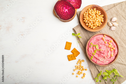 Hummus with beet and microgreen basil sprouts in wooden bowl on a white wooden background. Top view, copy space.