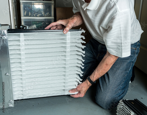 Senior caucasian man checking a clean folded air filter in the HVAC furnace system in basement of home