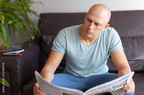 А serious man reading a newspaper at home on the couch