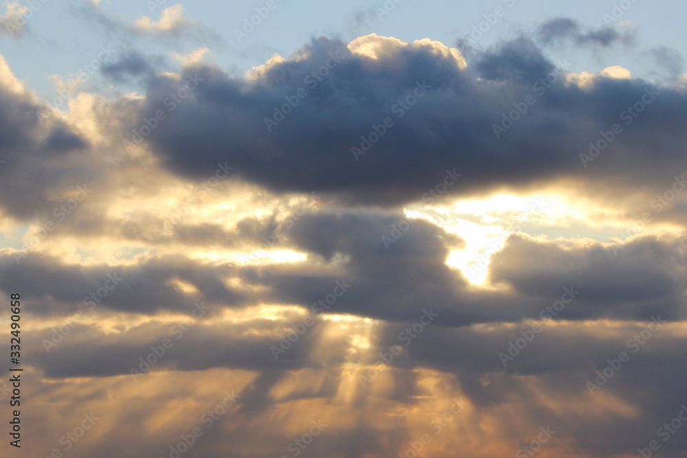 Obraz premium The sun at sunset or dawn behind the clouds, shines through. The sun's rays in the sky