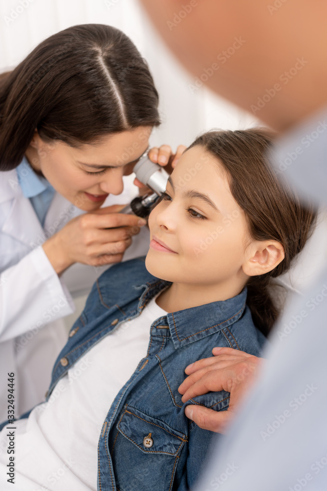 cropped view of father touching shoulder of daughter while otolaryngologist examining her ear with otoscope cropped view of father touching shoulder of daughter while otolaryngologist examining her ear with otoscope