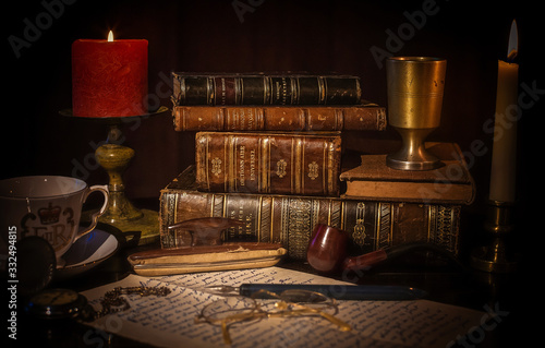 An old desk with a pile of vintage brown leather books, an open book with eye glasses, a cup of coffee, a red candle with flame, a vintage pocket clock, earth globe.