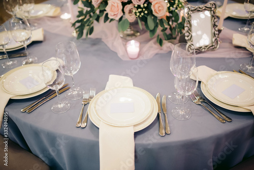 Elegant wedding table decorated with blue tablecloth, white plates and silver cutlery, candles and pink roses