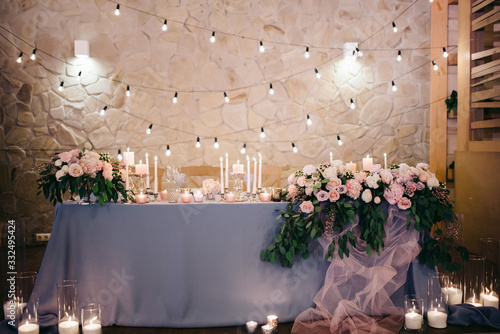 newlyweds wedding table decorated with blue tablecloth, plates, glasses, candles and flowers and green arrangements