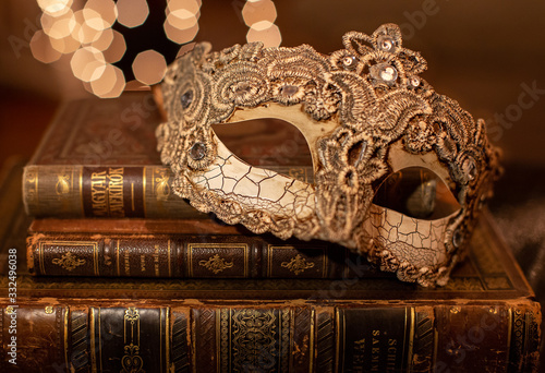A close up of a venetian lace mask with vintage patina on and an old brown book with bokeh background.