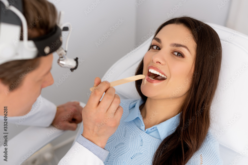 attractive woman looking at camera while ent physician holding tongue depressor attractive woman looking at camera while ent physician holding tongue depressor