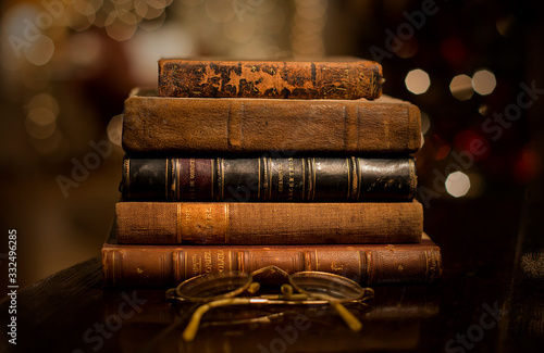 A vintage pile of five old brown leather books with eye glasses on a wood table.	