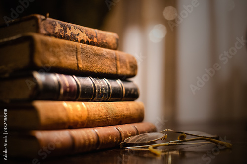 A vintage pile of five old brown leather books with eye glasses on a wood table. photo