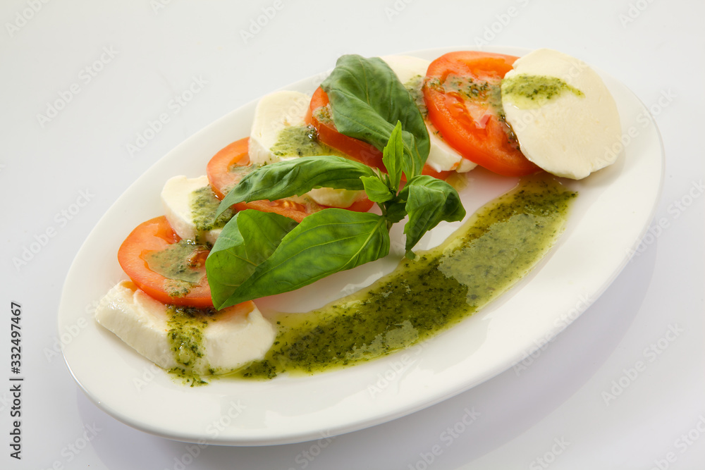 Caprese Salad with Tomatoes, Mozzarella Cheese, Rocket Salad, basil leaves, dressed with Pesto Sauce on rustic wooden background.  Traditional Italian cuisine. Flatlay healthy vegetarian dish.