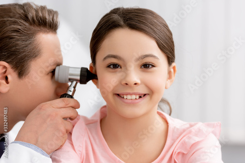 Foto ent physician examining ear of cheerful kid with otoscope