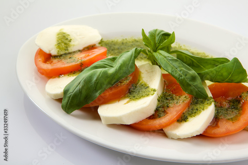 Caprese Salad with Tomatoes, Mozzarella Cheese, Rocket Salad, basil leaves, dressed with Pesto Sauce on rustic wooden background. Traditional Italian cuisine. Flatlay healthy vegetarian dish.