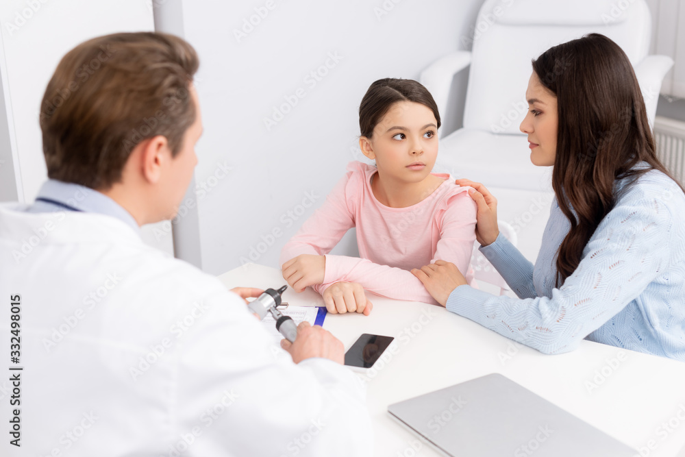 smiling mother touching daughters shoulder during consultation with ent physician smiling mother touching daughters shoulder during consultation with ent physician