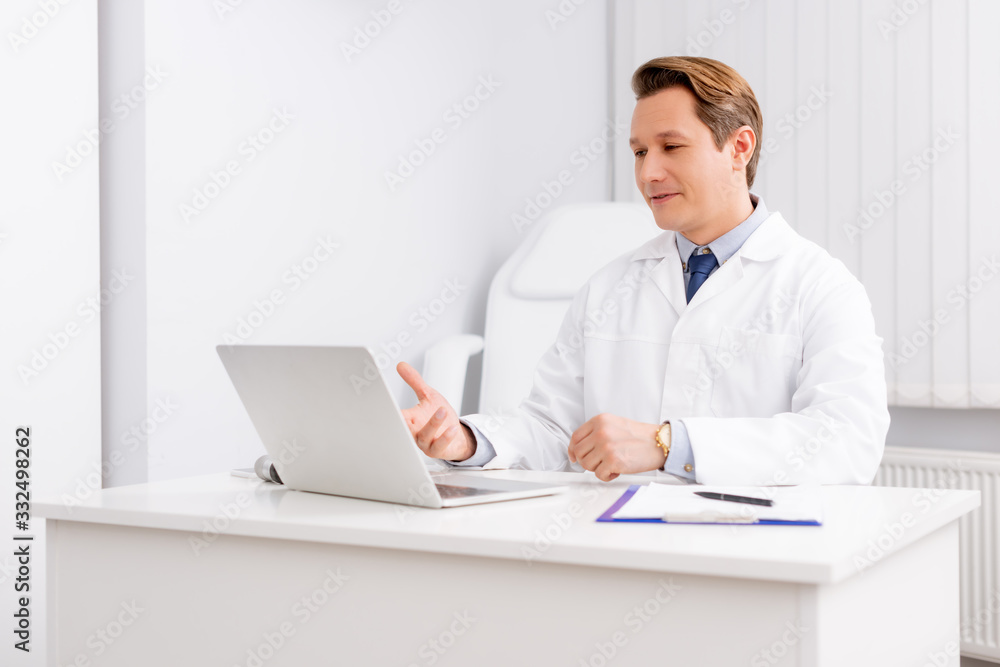 handsome otolaryngologist having video chat on laptop while sitting at workplace handsome otolaryngologist having video chat on laptop while sitting at workplace