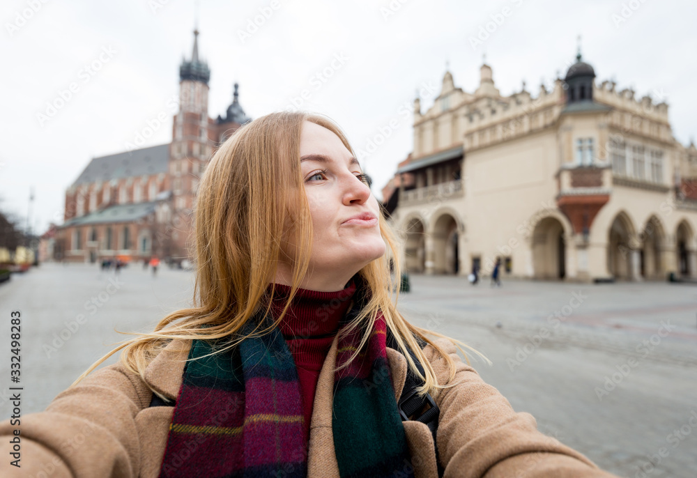 Stylish blonde woman tourist making selfie photo in front of the famous St. Mary's Basilica on the Market square. Travel concept and discovery of beautiful places. Krakow, Poland