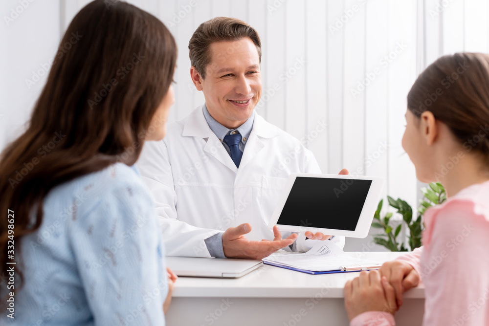 back view of mother and daughter looking at smiling ent physician showing digital tablet with blank screen back view of mother and daughter looking at smiling ent physician showing digital tablet with blank screen
