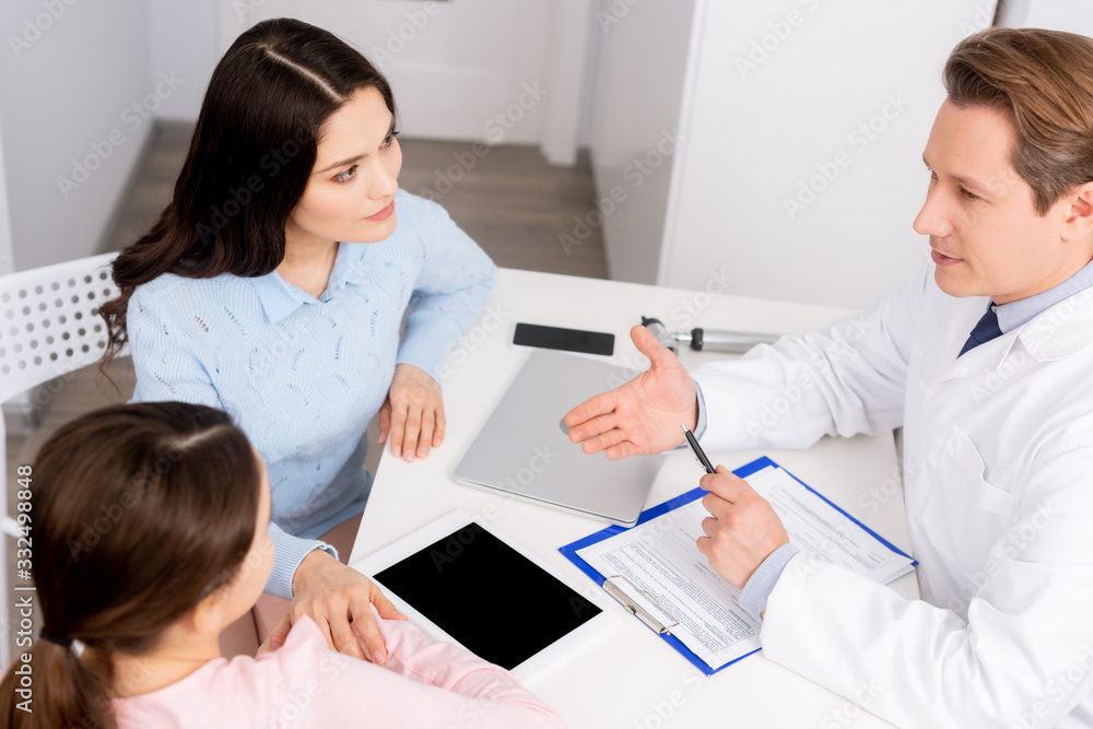 high angle view of otolaryngologist talking to mother and daughter near digital tablet with blank screen high angle view of otolaryngologist talking to mother and daughter near digital tablet with blank screen
