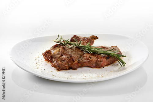 Grilled beef steak with rosemary. Grilled striploin sliced steak. Juicy thick grilled T-bone beef steak seasoned with rosemary fresh of the summer BBQ. Vegetables on a black plate with salt and pepper