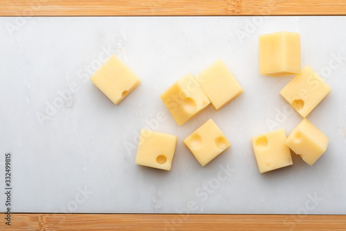 Portions (cubes, dice) of Emmental Swiss cheese . Texture of holes and alveoli. On white marble table.