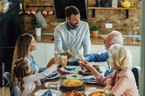 Happy multi-generation family toasting while having lunch together at home. © Drazen