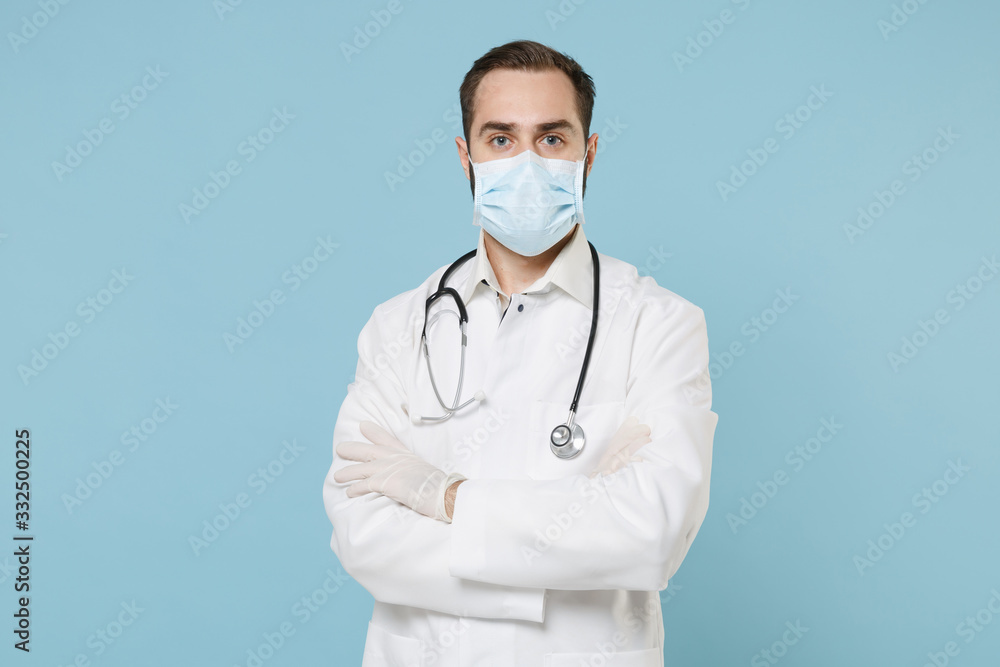 Male doctor man in white medical gown sterile face mask gloves isolated on blue background. Epidemic pandemic spreading coronavirus 2019-ncov sars covid-19 flu virus concept. Holding hands crossed. Male doctor man in white medical gown sterile face mask gloves isolated on blue background. Epidemic pandemic spreading coronavirus 2019-ncov sars covid-19 flu virus concept. Holding hands crossed.
