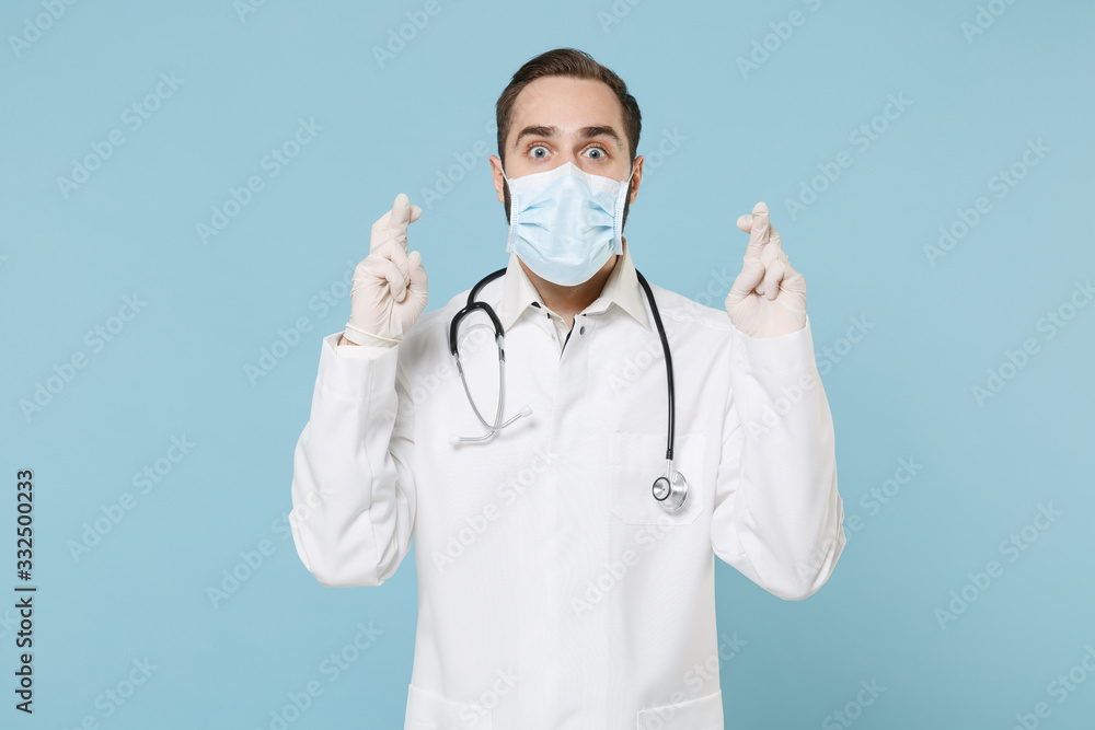 Male doctor man in medical gown sterile face mask gloves isolated on blue background. Epidemic pandemic coronavirus 2019-ncov sars covid-19 flu virus. Wait for special moment, keeping fingers crossed. Male doctor man in medical gown sterile face mask gloves isolated on blue background. Epidemic pandemic coronavirus 2019-ncov sars covid-19 flu virus. Wait for special moment, keeping fingers crossed.